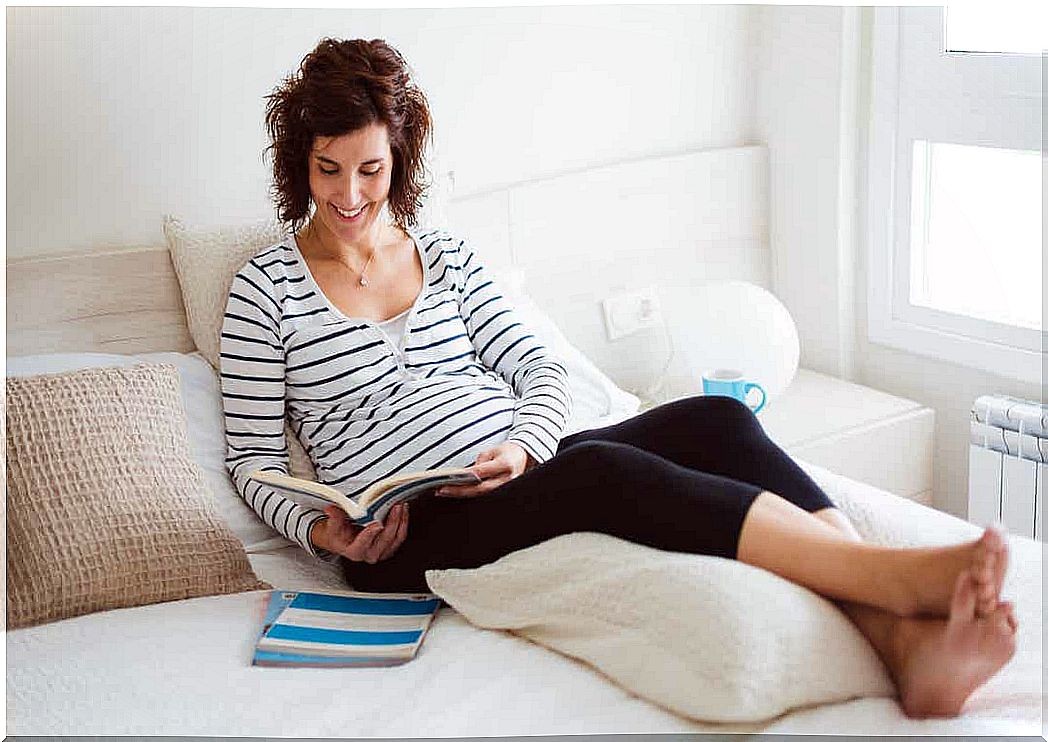 A pregnant woman reading a book of names in bed.