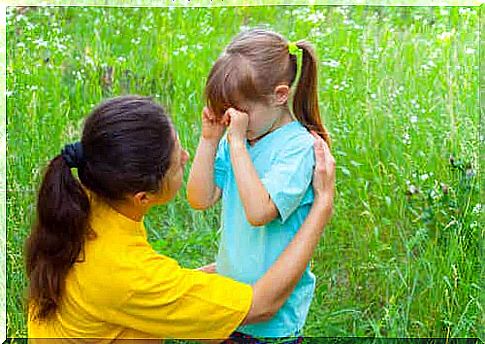 A mother kneeling to comfort her crying daughter.