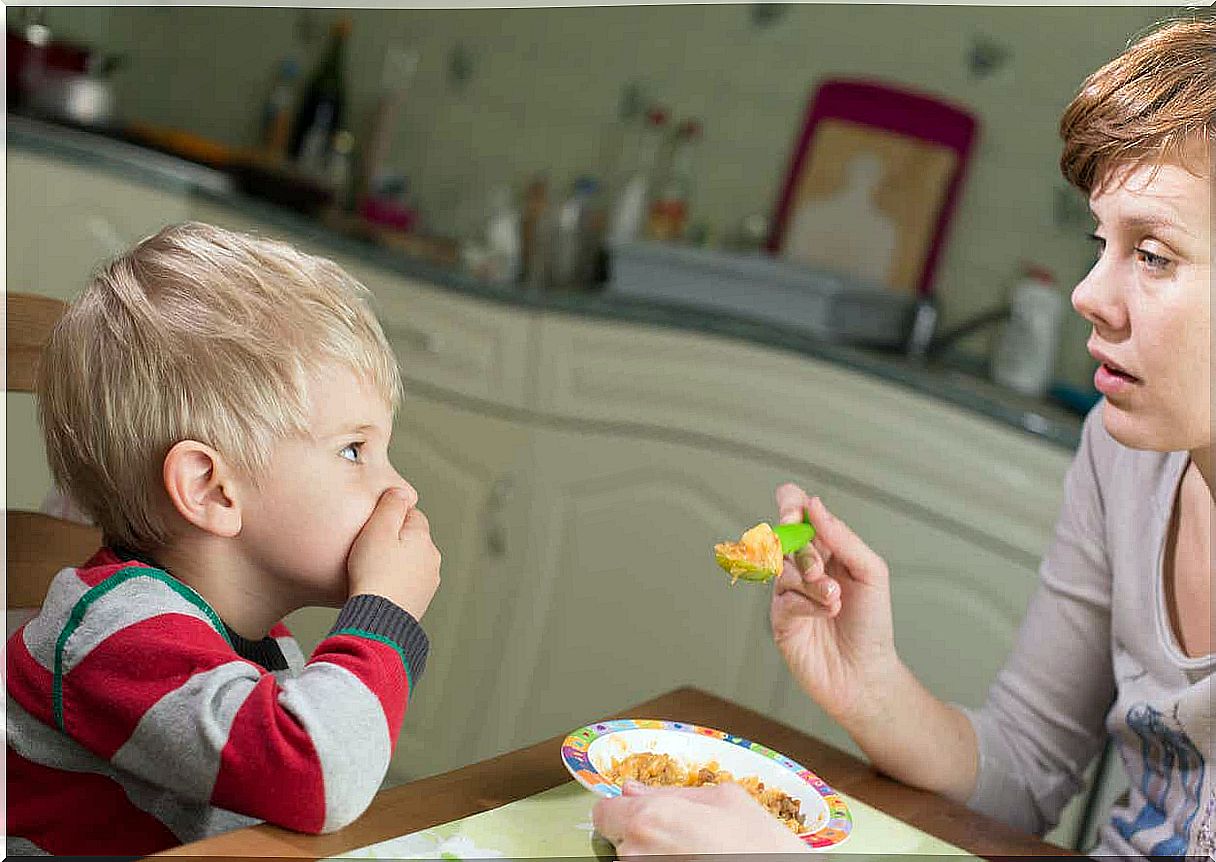 A young child covers his mouth as his mother tries to feed him.