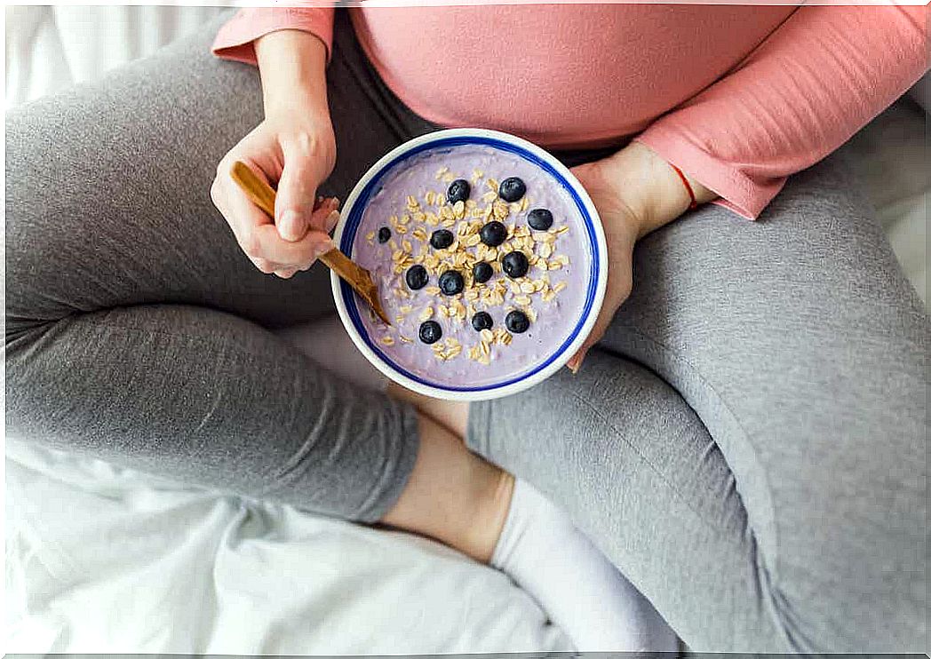 A pregnant woman eating granola with yogurt and fruit.