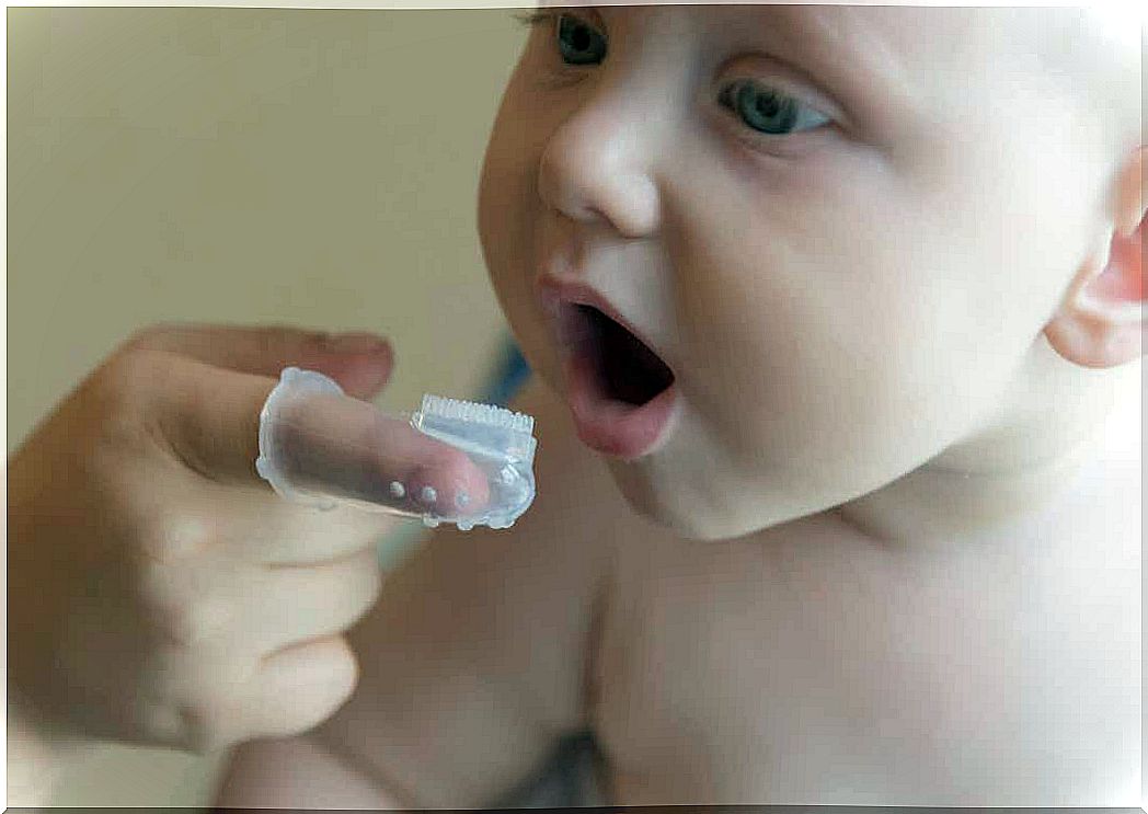 A mother using a finger brush to clean her baby's gums.