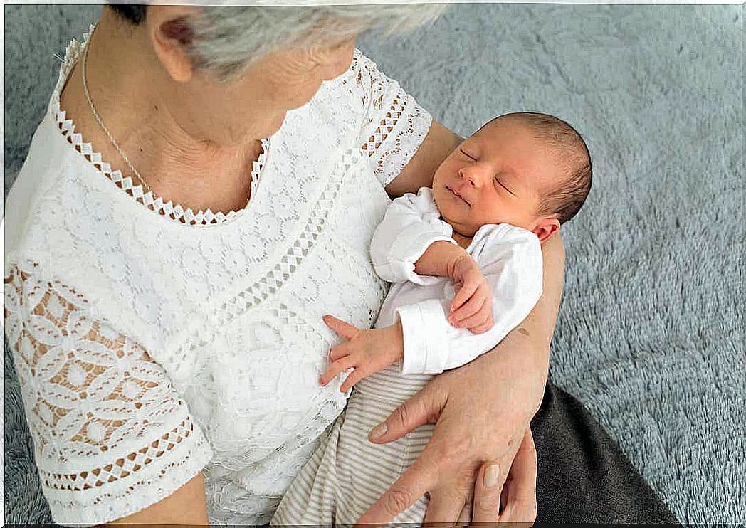 A grandmother looking down at her newborn grandchild in her arms.