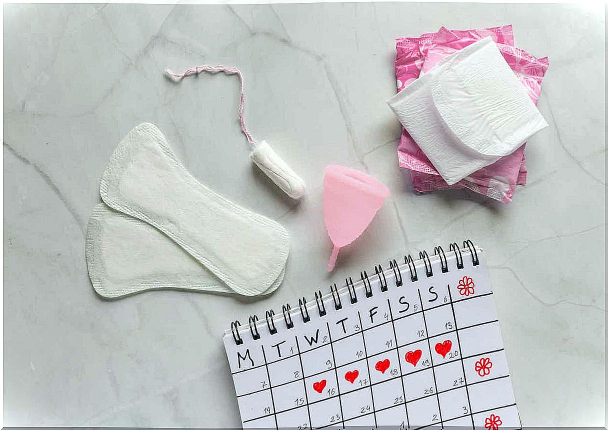 A calendar and various feminine hygiene products, including pads, pantyliners, a tampon, and a menstrual cup.