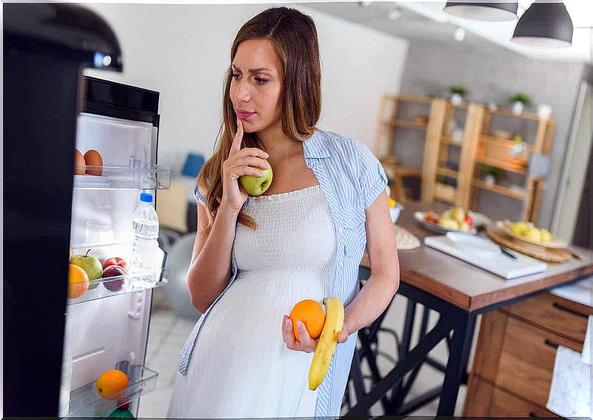 A pregnant woman takes fruit from the refrigerator.