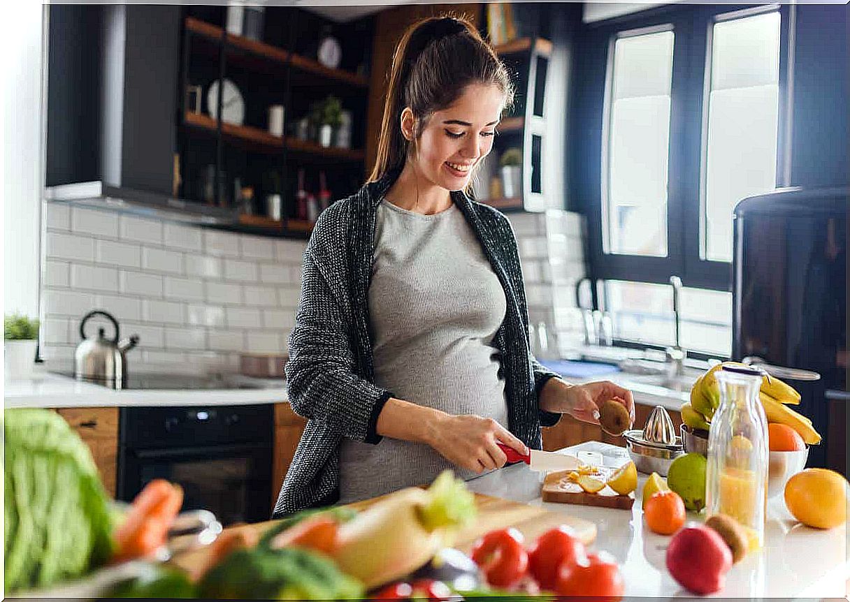 A pregnant woman cutting fresh fruit.