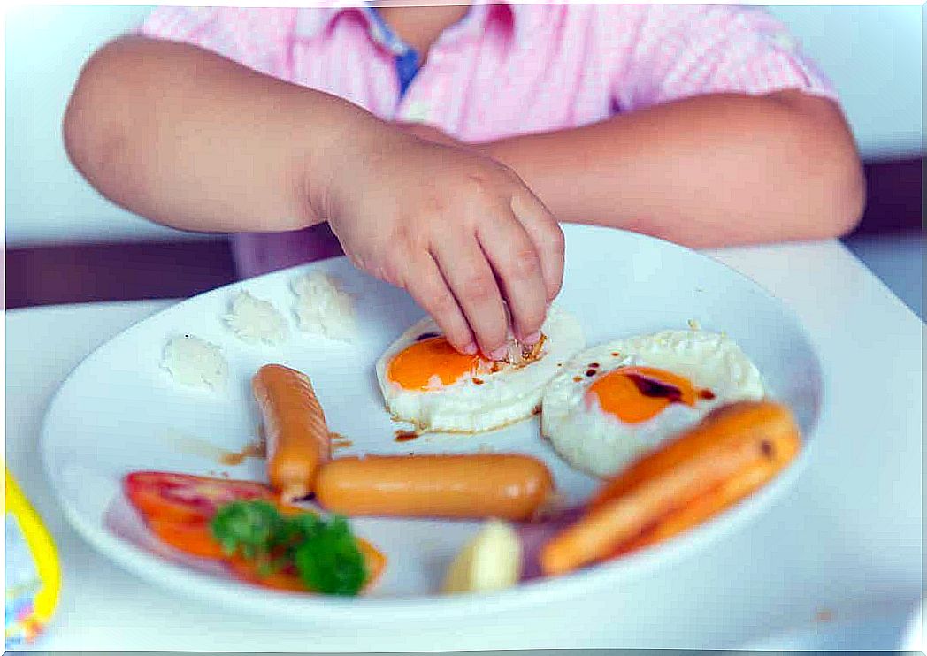 A child eating eggs and sausages.